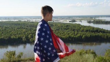 Sarışın çocuk nehir kıyısında mavi gökyüzünde ulusal Amerikan bayrağı sallıyor.