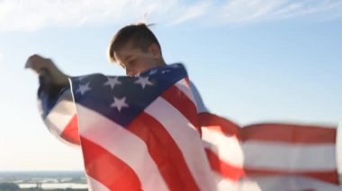 Sarışın çocuk nehir kıyısında mavi gökyüzünde ulusal Amerikan bayrağı sallıyor.