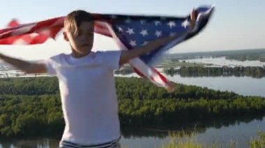 Sarışın çocuk nehir kıyısında mavi gökyüzünde ulusal Amerikan bayrağı sallıyor.