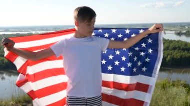 Nehir kıyısında mavi gökyüzünde ulusal Amerikan bayrağı sallayan bir çocuk.