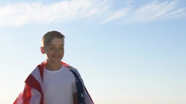 Boy waving national USA flag outdoors over blue sky at the river bank — Stock Video