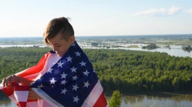 Nehir kıyısında mavi gökyüzünde ulusal Amerikan bayrağı sallayan bir çocuk.