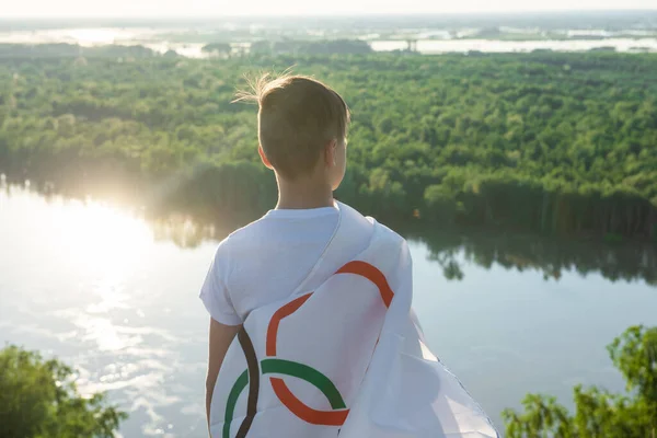 Blond pojke viftande flagga de olympiska spelen utomhus över blå himmel vid floden stranden — Stockfoto