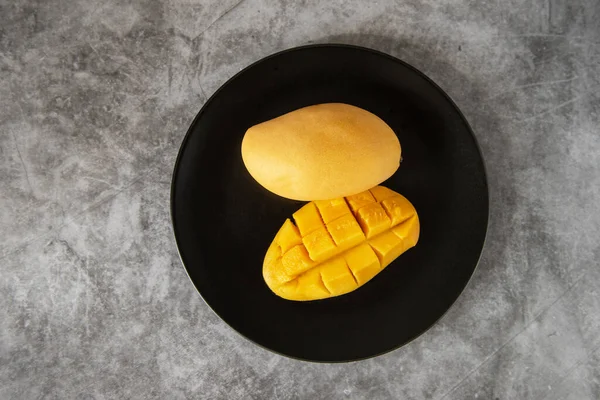 Frutta fresca di mango giallo in un piatto nero — Foto Stock