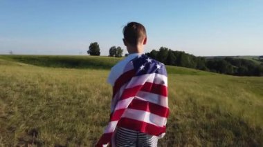 Nehir kıyısında mavi gökyüzünde ulusal Amerikan bayrağı sallayan bir çocuk.