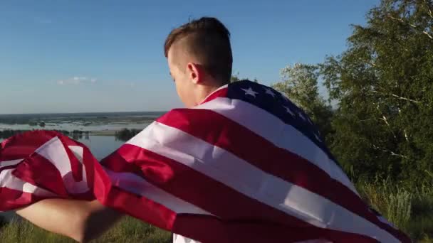 Pojke viftar nationell USA flagga utomhus över blå himmel vid floden banken — Stockvideo