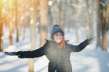 Mutlu genç kadın kışın güneşli parkta kar atıyor.