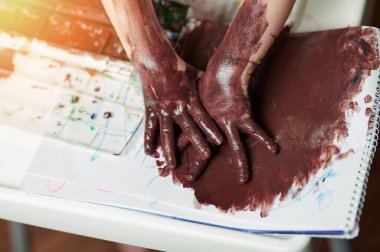 Çocuk kirli avuçlarıyla kağıt üzerinde parmak izi bırakıyor.