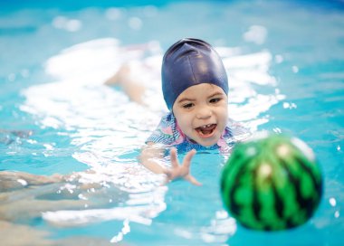 Yüzen bebek topu mavi havuz suyunda yakalamaya çalışıyor. Etkin tatil teması