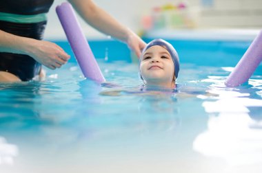 Yüzen çocuk, yüzen kız ve öğretmeniyle bulanık arka planda yardım ediyor.