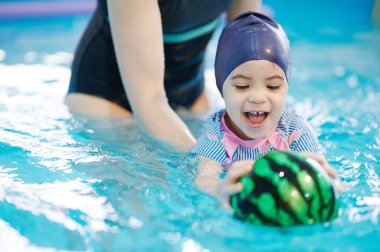 Çocuk mavi su arka planında yüzme dersinde topu yakalıyor.