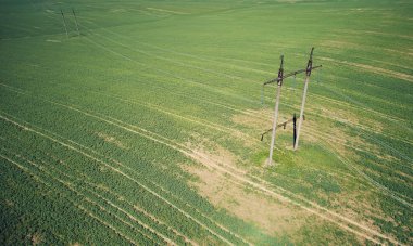 Yeşil çayır arkaplanındaki yüksek voltajlı elektrik hattı kuleleri üst görünümün üzerindeki hava sahası