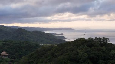 Alacakaranlıkta çarpıcı kıyı manzarasının tadını çıkarın. Bereketli dağların ve bulutlu gökyüzünün altındaki sakin okyanusun tadını çıkarın..