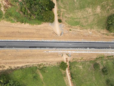 Kırsal alandaki tarlalardan ve ağaçlardan geçen yeni asfalt bir yol manzarası.