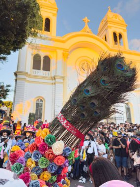 Diriamba, Nikaragua - 22 Ocak 2026: Kilise arka planında ulusal Nikaragua kostümü giymiş tavus kuşu tüylü uzun renkli maske