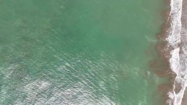 Güneşli bir günde sahile vuran dalgalar berrak suyla birlikte. İnsanlar etraflarında güneşin ve doğanın tadını çıkarırlar..