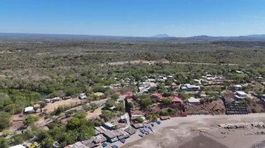 Güneşli bir günde yeşil ağaçlar ve dağlarla çevrili küçük bir kasabanın hava manzarası. Kasabanın birçok evi ve yolu var..