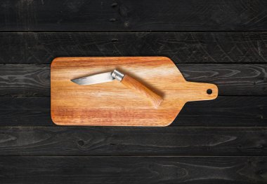 Ahşap kesme tahtası ve çakı siyah tahta masa arkasında.