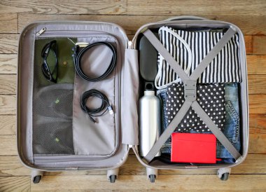 Tahta arka planda izole edilmiş giysilerle dolu bir valizi aç.