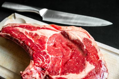 Siyah arka planda soyutlanmış bir kesme tahtasının üzerinde çiğ et ve bıçak..