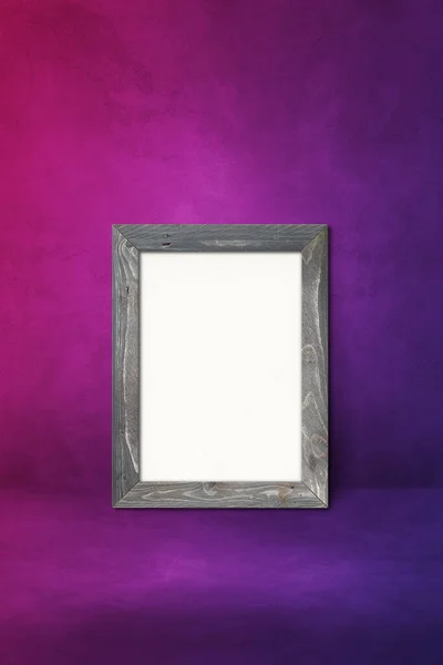 Wooden picture frame leaning on a purple wall. Blank mockup template