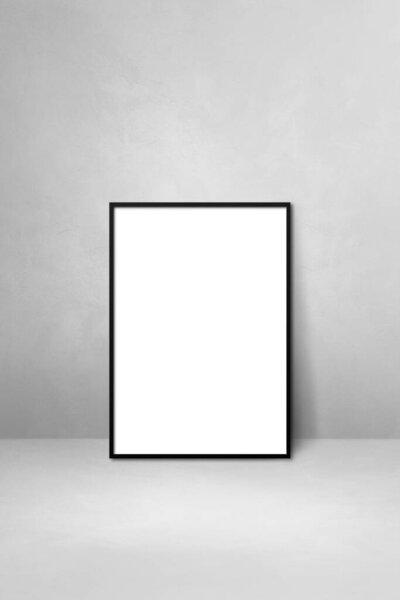 Black picture frame leaning on a light grey wall. Blank mockup template