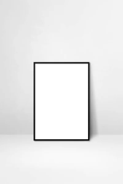 Black picture frame leaning on a white wall. Blank mockup template