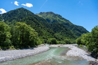 Azusa Nehri, Japon Alpleri 'ndeki Kamikochi yürüyüş parkurunun karla kaplı tepelerinin altındaki yemyeşil ormanlarda esiyor.