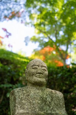 Hiroşima 'daki Mitaki-Dera Tapınağı' nda orman gölgesiyle çevrili yıpranmış bir heykel huzur içinde duruyor.