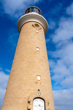 Cape Du Couedic deniz feneri Avustralya 'nın Kanguru Adası' ndaki Flinders Chase Ulusal Parkı 'nda kıyı bitkilerinin arasında yer alır. Kırmızı ve beyaz tepesi bulutlu gökyüzü ile çelişiyor.