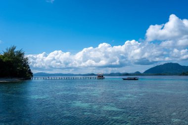 Bolilanga Adası, Togian takımadaları, Sulawesi, Endonezya 'nın sakin sularına doğru uzanan uzun ve ahşap bir iskele mavi gökyüzünün altında bir tekne.