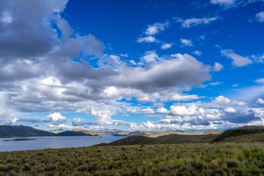 Peru 'daki Lagunillas Gölü, üzerinde kara fırtına bulutları ve dağların üzerine yağan yağmur yağmuru ile yuvarlanan tepeler ve otlaklarla çevrilidir.
