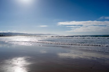 A vast sandy beach stretches along the Great Ocean Road, Australia, with gentle waves lapping the shore under a partly cloudy sky