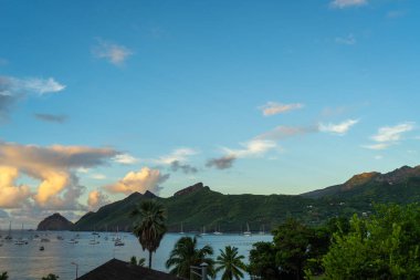 Nuku Hiva, Marquesas Adaları 'ndaki Taiohae Körfezi' nin üzerindeki gökyüzü, bereketli dağların yakınında yelkenlilerin demirlediği sakin okyanusu yansıtan ılık günbatımı renkleriyle parıldıyor. Fransız Polinezyası