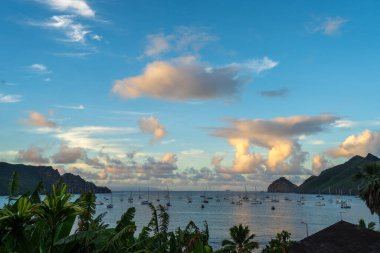 Nuku Hiva, Marquesas Adaları 'ndaki Taiohae Körfezi' nin üzerindeki gökyüzü, bereketli dağların yakınında yelkenlilerin demirlediği sakin okyanusu yansıtan ılık günbatımı renkleriyle parıldıyor. Fransız Polinezyası