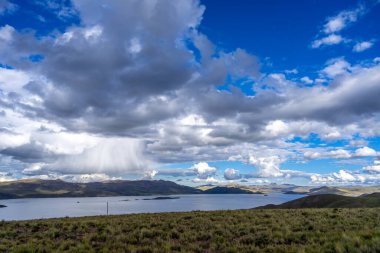 Peru 'daki Lagunillas Gölü, üzerinde kara fırtına bulutları ve dağların üzerine yağan yağmur yağmuru ile yuvarlanan tepeler ve otlaklarla çevrilidir.