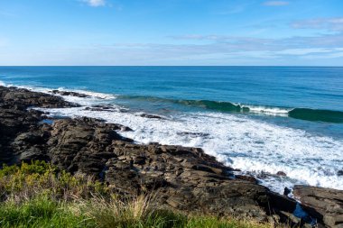 Avustralya 'daki Büyük Okyanus Yolu boyunca uzanan kayalık sahil şeridinde engebeli siyah kayalar, dalgalar ve engin mavi bir okyanus bulunur. Köpüklü beyaz sörf kıyıya çarpar ve dinamik ve manzaralı bir kıyı manzarası yaratır.