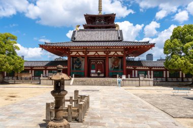 Bir adam, Osaka 'daki Shitenno-ji Tapınağı' nın ana kapısının önünde dua ediyor. Orada, geleneksel mimari ve ruhsal atmosfer parlak bir gökyüzünün altında buluşuyor.