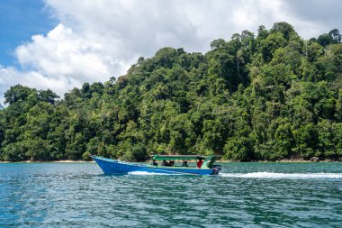 Küçük bir tekne Endonezya 'nın Sulawesi kentindeki Togian Adaları' nın yemyeşil bir adası yakınlarındaki mavi sulardan geçiyor.