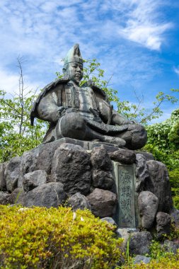 Şogun Minamoto no Yoritomo 'nun bronz heykeli yeşil ve gökyüzü ile çevrili Genjiyama Park, Kamakura' daki taş bir üste zırh içinde oturuyordu.