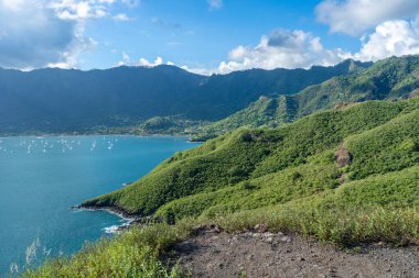 Nuku Hiva, Marquesas Adaları 'ndaki Taiohae Körfezi, kıyı kenti yakınlarındaki sakin sularda demirlemiş yelkenli tekneleriyle mavi ve bulutlu bir gökyüzünün altında yeşil dağlarla çevrilidir. Fransız Polinezyası