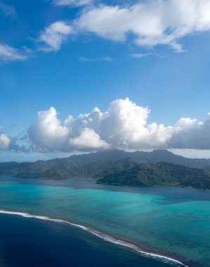 Fransız Polinezyası 'ndaki Tahaa adası, yukarıdan bakıldığında turkuaz bir göl, mercan resifi ve yemyeşil dağları ortaya çıkarır. Canlı okyanus renkleri koyu mavi Pasifik ile tezat oluşturuyor.