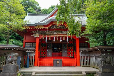 Enoshima-Shrine Nakatsunomiya 'nın parlak kırmızı ana salonu Japonya' nın Enoshima Adası 'ndaki ağaçlar, geleneksel fenerler ve koruyucu heykellerle çevrilidir.