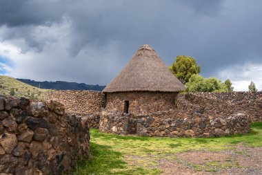 Peru 'daki Raqchi' nin tarihi mekanında antik İnka taş duvarları ve yeşil manzaralar ve And Dağları ile çevrili yeniden inşa edilmiş sazdan çatı kulübesi yer alıyor.