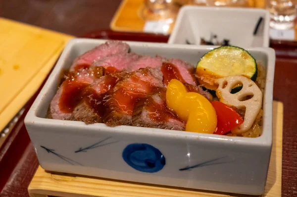 Sosla kaplı sulu Wagyu bifteği dilimleri, Miyajima adasında geleneksel bir seramik kutuda sebze ve pirinç ile servis edilir.