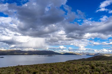 Peru 'daki Lagunillas Gölü, üzerinde kara fırtına bulutları ve dağların üzerine yağan yağmur yağmuru ile yuvarlanan tepeler ve otlaklarla çevrilidir.