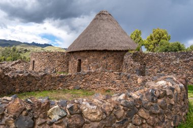 Peru 'daki Raqchi' nin tarihi mekanında antik İnka taş duvarları ve yeşil manzaralar ve And Dağları ile çevrili yeniden inşa edilmiş sazdan çatı kulübesi yer alıyor.