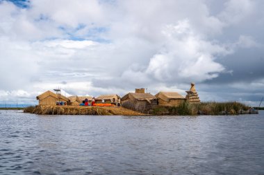 Peru, Titicaca Gölü 'ndeki yüzen Uros Titino adası, parlak bir gökyüzünün altında derin mavi sularla çevrili kamış evleri, demirlemiş tekneler ve yemyeşil bitki örtüsüne sahiptir.