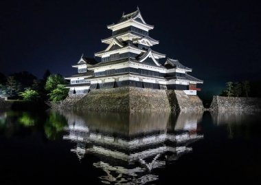 Yumuşak ışıklarla aydınlatılan Matsumoto Şatosu geceleri görkemli bir şekilde duruyor. Karanlık silueti etrafındaki hendeğe yansıyor.