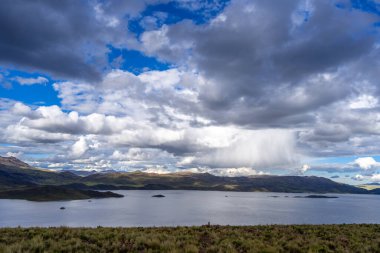 Peru 'daki Lagunillas Gölü, üzerinde kara fırtına bulutları ve dağların üzerine yağan yağmur yağmuru ile yuvarlanan tepeler ve otlaklarla çevrilidir.